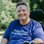 Huhana Hickey in her wheelchair, wearing a shirt that says "The future is accessible"