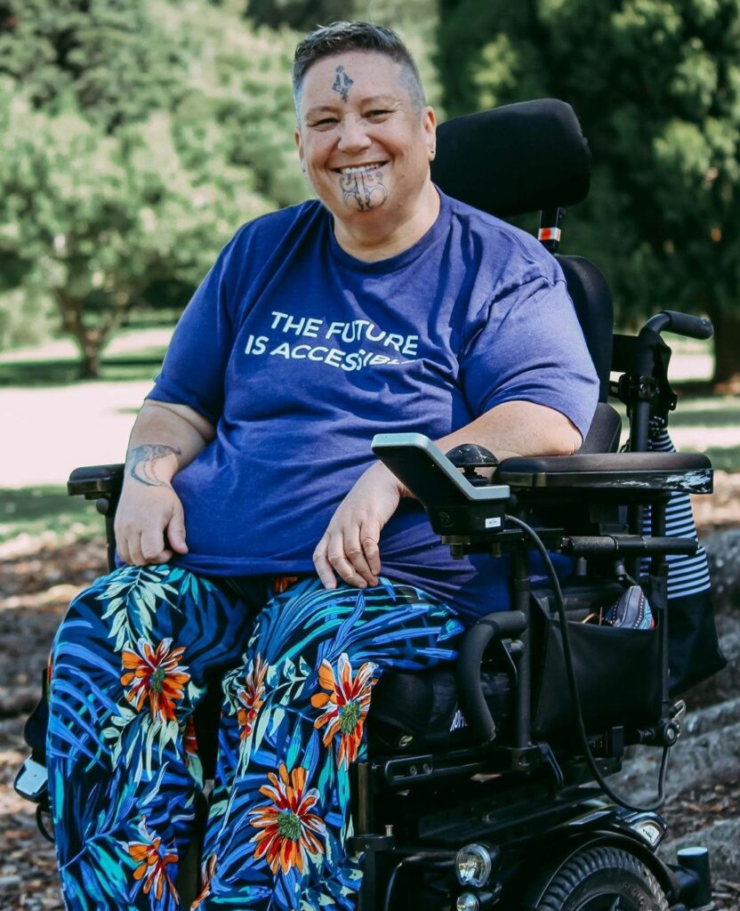 Huhana Hickey in her wheelchair, wearing a shirt that says "The future is accessible"